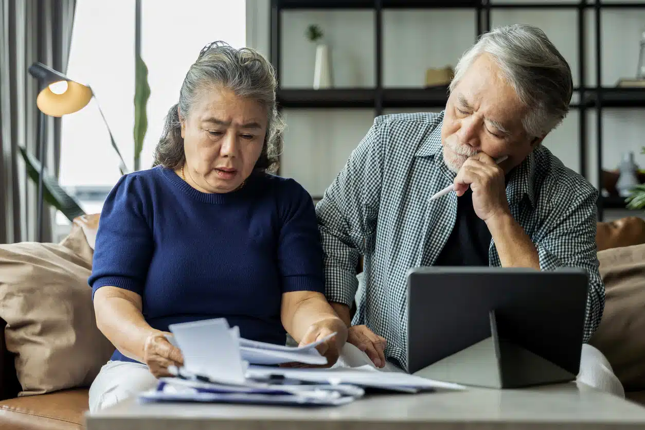 Serious stressed asian senior old couple worried about bills discuss unpaid bank debt paper, sad poor retired family looking at tablet counting loan payment worry about money problem
